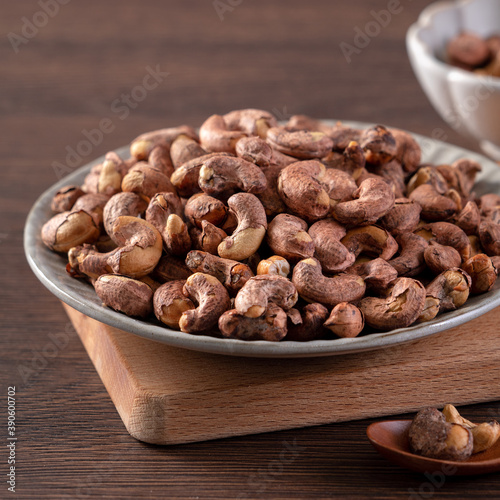 Cashew nuts with peel in a plate on wooden tray.