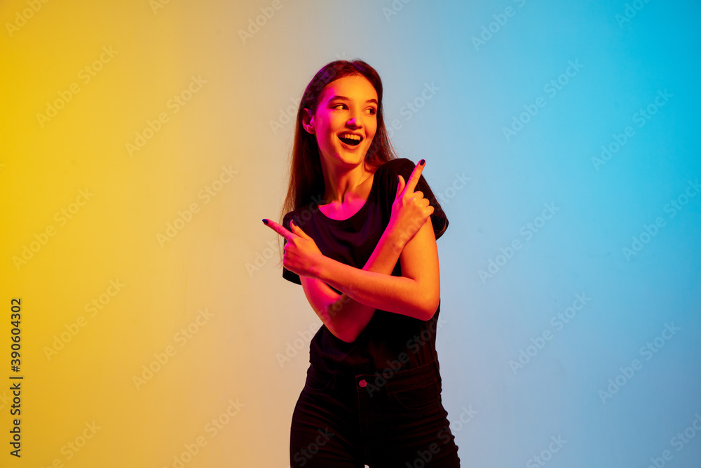 © master1305 - Pointing, laughting. Young caucasian woman's portrait on gradient blue-yellow studio background in neon light. Concept of youth, human emotions, facial expression, sales, ad. Beautiful brunette model. © master1305 - Pointing, laughting. Young caucasian woman's portrait on gradient blue-yellow studio background in neon light. Concept of youth, human emotions, facial expression, sales, ad. Beautiful brunette model.