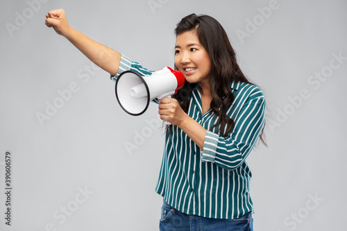 communication, feminism and human rights concept - happy smiling asian young woman speaking to megaphone over grey background