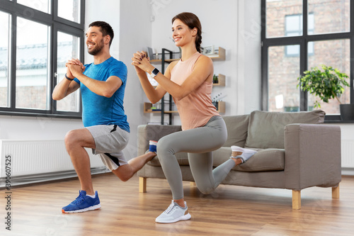 sport, fitness, lifestyle and people concept - smiling man and woman exercising and doing squats in low lunge at home