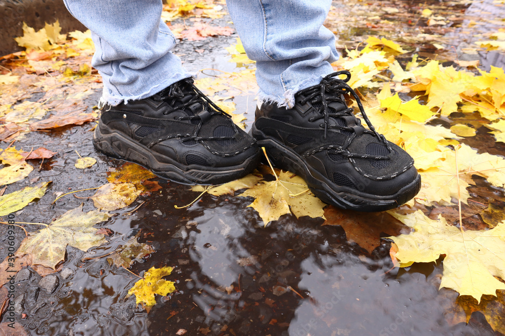 feet in sneakers stand on the autumn sidewalk, leaves in a puddle