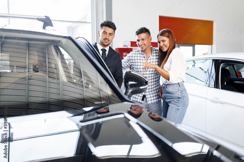 Young couple choosing a car at the dealership with manager helping Young couple choosing a car at the dealership with manager helping