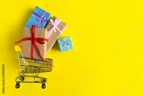 Empty shopping grocery cart with gifts on yellow background. Concept of business, shopping, black friday sales. Top view or flat lay composition