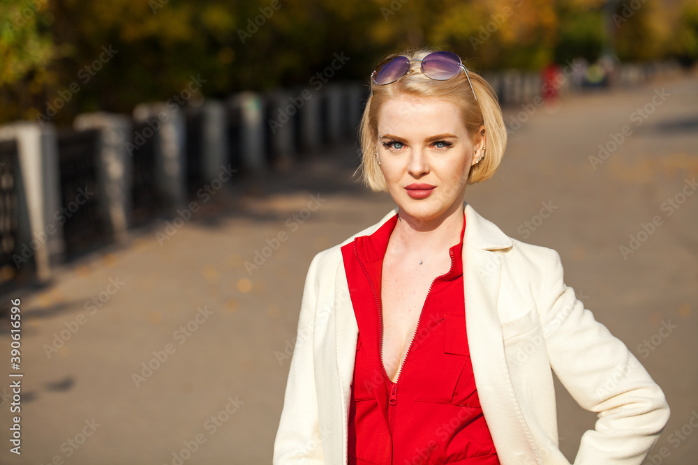 Young beautiful woman in a beige coat walks in the autumn park