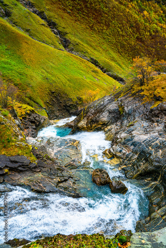 Wild and twisting waterfall flowing down a mountain slope in lush yellow and green autumn colors.