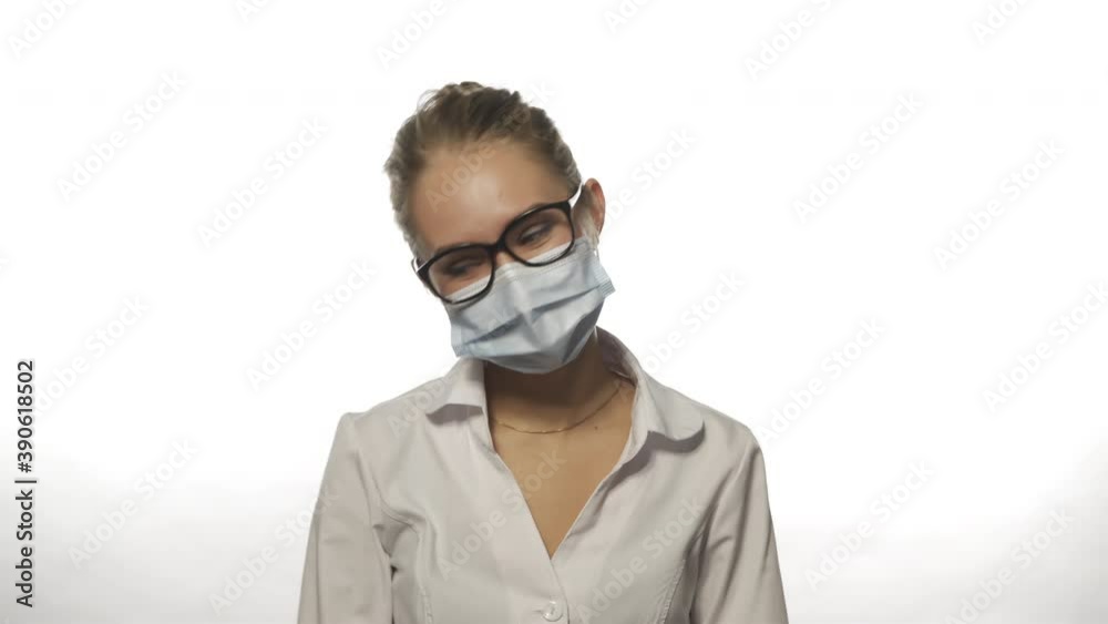 Funny nurse in mask on white background with glasses blinks and laughs looking straight at camera. Caucasian young woman waving hands in medical gloves. Anti-stress concept. High quality 4k footage Funny nurse in mask on white background with glasses blinks and laughs looking straight at camera. Caucasian young woman waving hands in medical gloves. Anti-stress concept. High quality 4k footage