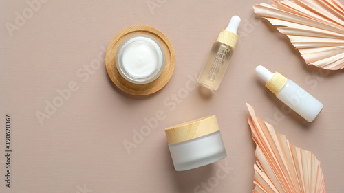Set of natural cosmetic products on beige background. Flat lay organic body cream, serum and essential oil in dropper bottles, dry flowers leaves on beige background. SPA natural beauty products.