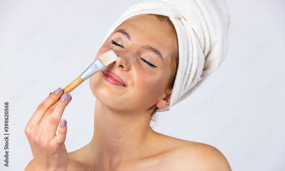 A girl with a towel on her head and hangs on her face, applies a gel mask with a brush. Fashionable female model with beautiful appearance. Photo on white background