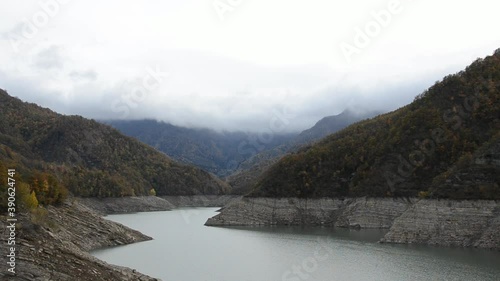 Clouds float over the tops of the mountains with autumn forest and lake
