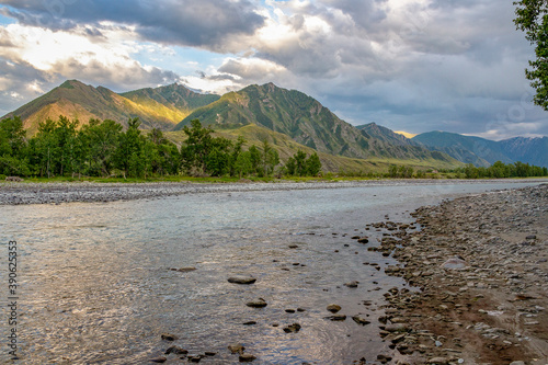 The river is set against the backdrop of partially sunlit mountains and beautiful clouds