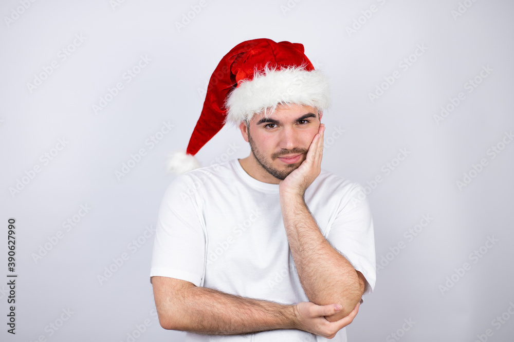Young handsome man wearing a Santa hat over white background thinking looking tired and bored with crossed arms