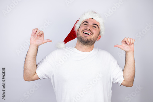 Young handsome man wearing a Santa hat over white background looking confident with smile on face, pointing oneself with fingers proud and happy.