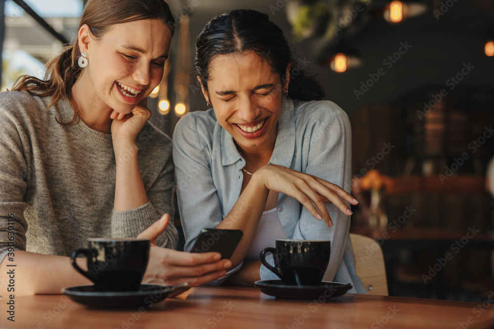 Friends using a cellphone and smiling at cafe Friends using a cellphone and smiling at cafe
