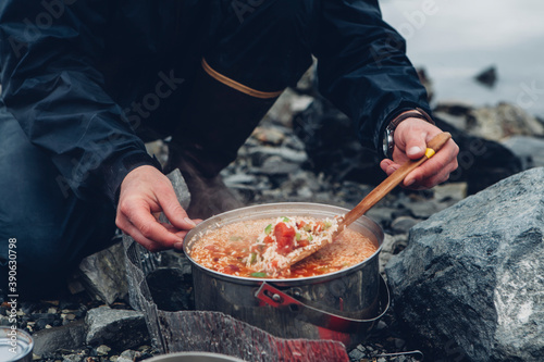 A wild camper stirring hot food in a pot cooking over a fire.  photo