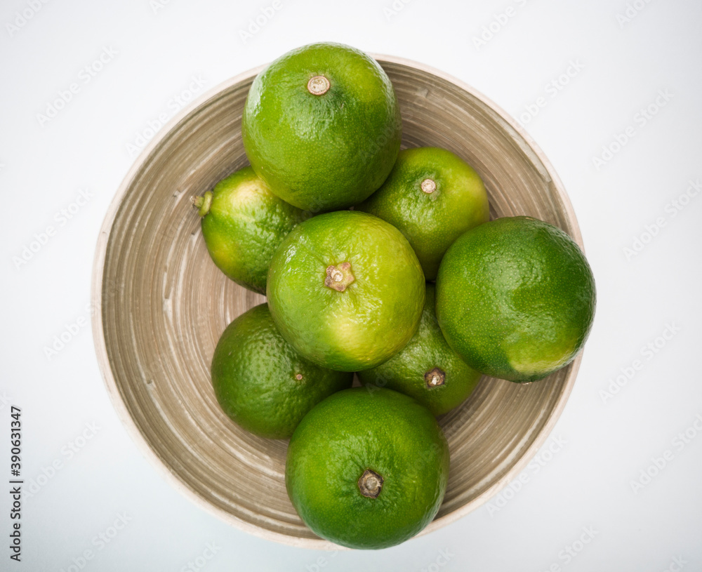 Top view of bowl with green limes and mint leafs inside on the white background. Juicy colorful fruits for mojito. Freshness and health. Top view of bowl with green limes and mint leafs inside on the white background. Juicy colorful fruits for mojito. Freshness and health.