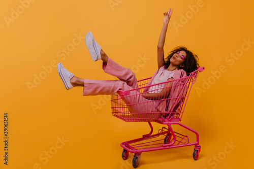 Enthusiastic brunette girl expressing sincere positive emotions. Studio shot of beautiful woman sitting in shopping cart. photo