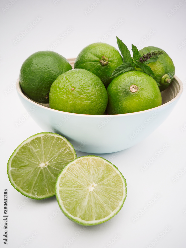 Light blue bowl with limes inside and a lime cut in half on the white background. Juicy, fresh and colorful fruits.