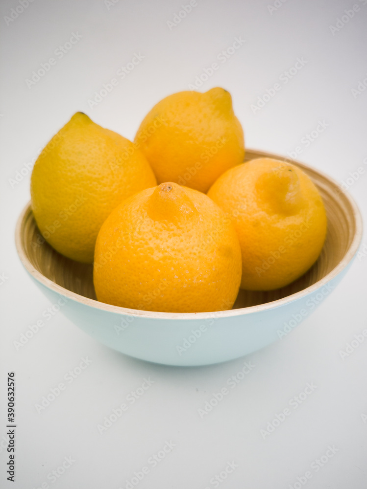 Light blue bowl with yellow lemons inside and a lemon next to it on the white background. Juicy, fresh and colorful fruits. Light blue bowl with yellow lemons inside and a lemon next to it on the white background. Juicy, fresh and colorful fruits.