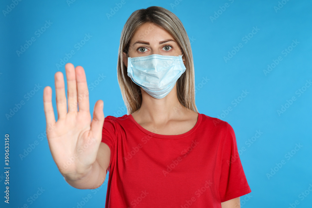 Woman in protective mask showing stop gesture on light blue background. Prevent spreading of coronavirus Woman in protective mask showing stop gesture on light blue background. Prevent spreading of coronavirus