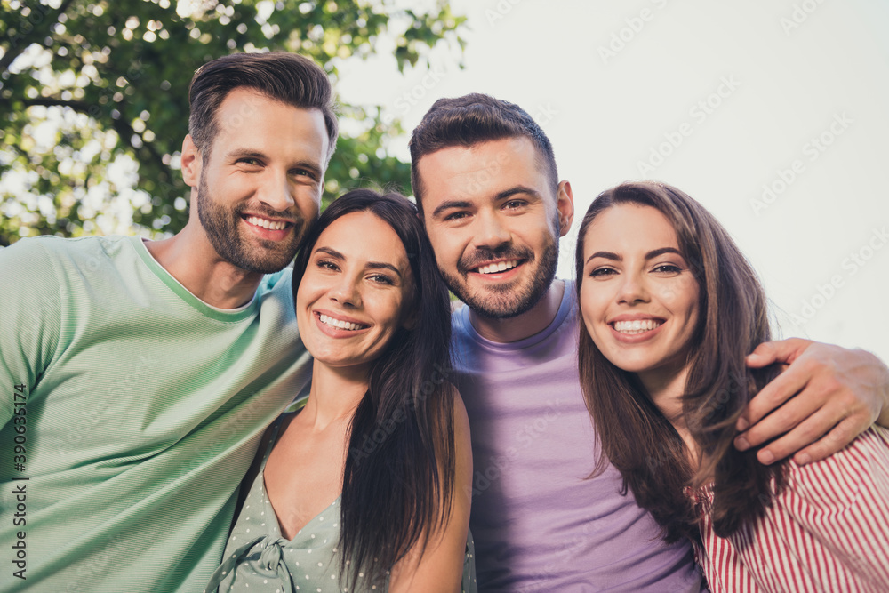 Low angle view photo of four happy friends men and women hug beaming smile good mood outside in outdoors Low angle view photo of four happy friends men and women hug beaming smile good mood outside in outdoors