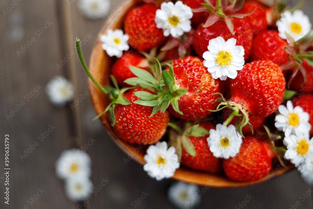 Сlose up image of yummy delicious big red strawberry with flowers lie in round wooden plate on light wooden background, antioxidant nutrition, healthy food concept Сlose up image of yummy delicious big red strawberry with flowers lie in round wooden plate on light wooden background, antioxidant nutrition, healthy food concept