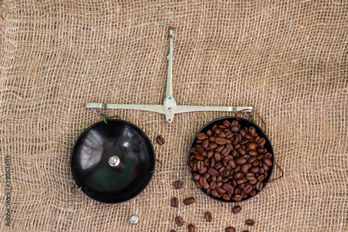 Fototapeta Naklejka Na Ścianę i Meble -  Roasted coffee beans, weighed on an antique hand scale with weights, lying on a table covered with burlap.
