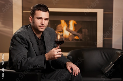 Man sitting in armchair at home, smelling wine, smiling.