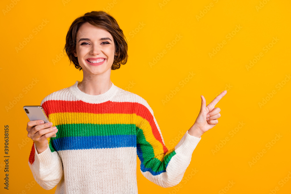 Photo of cheerful young girl hold telephone indicate finger empty space wear striped sweater isolated yellow color background Photo of cheerful young girl hold telephone indicate finger empty space wear striped sweater isolated yellow color background