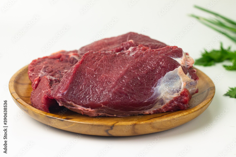 Close of view of slices fresh beef on wooden brown plate, with green celery and spring onion. White isolated background. 