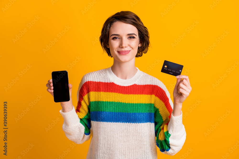 Photo of lovely girl hold debit card phone present screen empty space wear striped sweater isolated yellow color background Photo of lovely girl hold debit card phone present screen empty space wear striped sweater isolated yellow color background