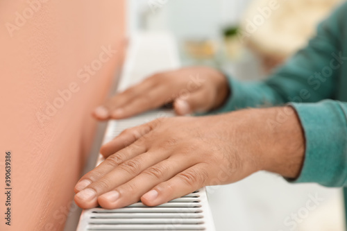 Man warming hands on heating radiator indoors  closeup