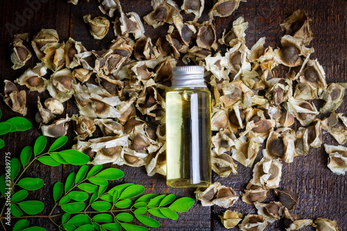 Oil of Moringa in bottle, green leaves and seeds on wooden background. Moringa oleifera tropical herb product concept. 