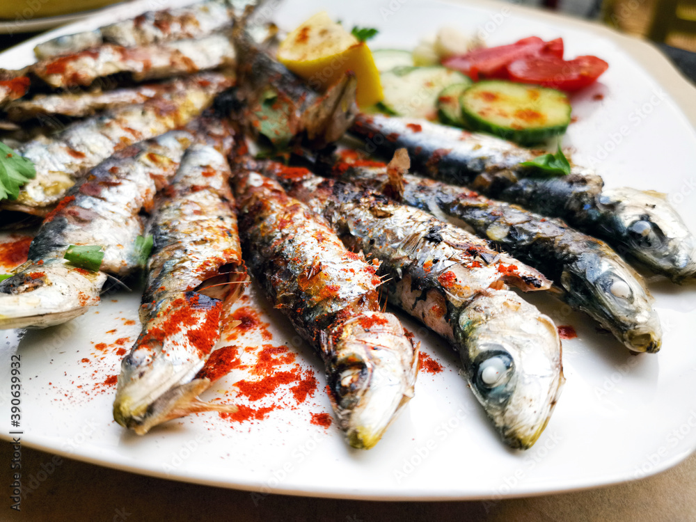 Fresh Grilled sardines served with fresh tomatoes, cucumbers slices and lemon on white plate for mediterranean healthy meal