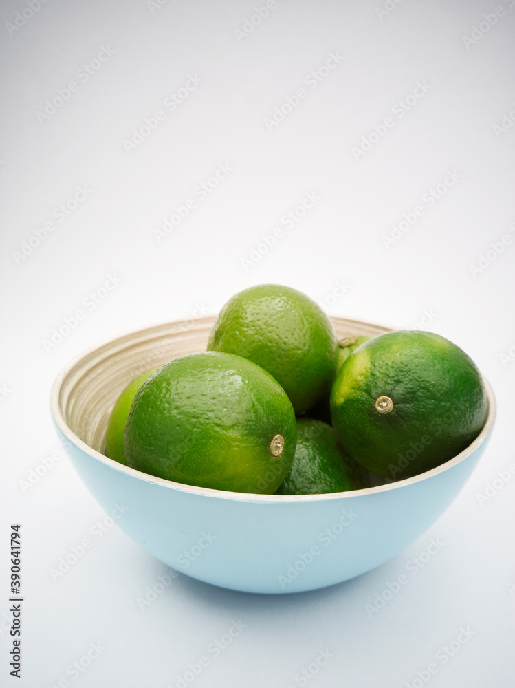 Light blue bowl with green limes inside on the white background. Juicy colorful fruits for mojito. Freshness and health. Light blue bowl with green limes inside on the white background. Juicy colorful fruits for mojito. Freshness and health.
