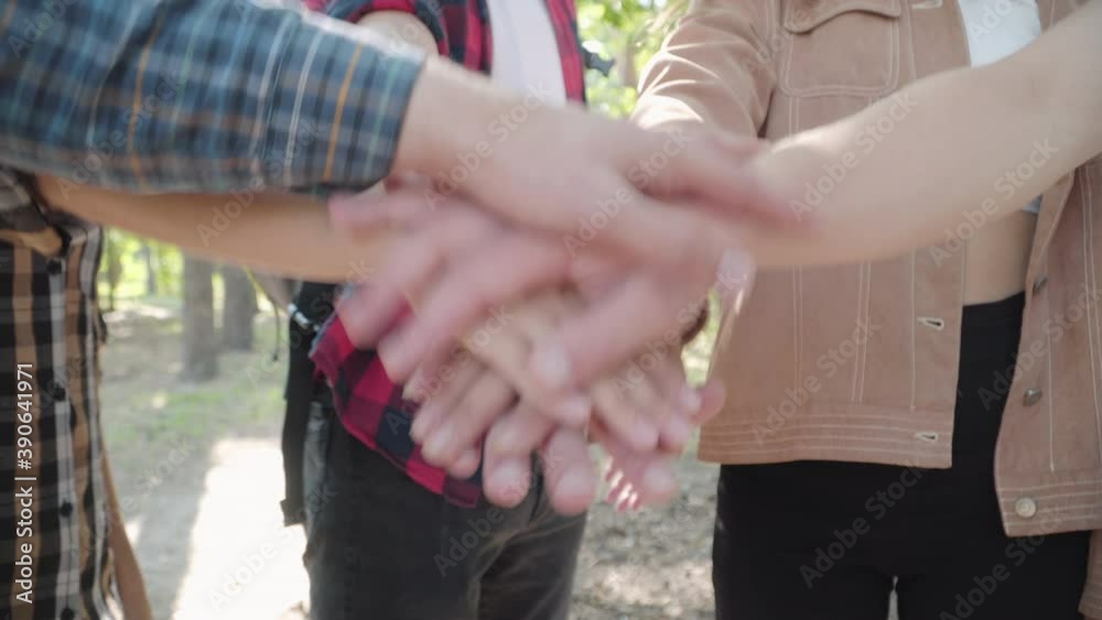 Close-up of unrecognizable Caucasian friends stacking hands in sunny forest outdoors. Group of positive men and women enjoying hiking outdoors in summer. Friendship and travelling concept.