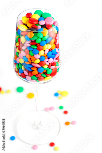 A wine glass full of colorful chocolate dragees, isolated on white. Studio photo. Selective focus. photo