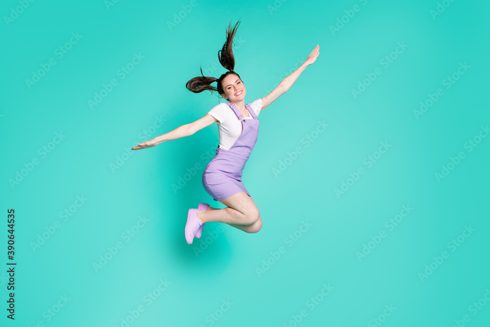 Full length photo of funky positive girl jump plane pose wear purple mini overall footwear isolated teal color background