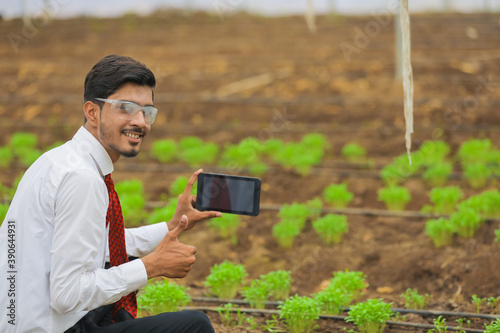 Technology and people concept, Young indian agronomist using tablet or smartphone at greenhouse