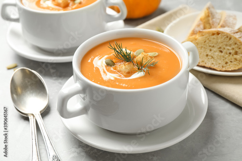 Tasty creamy pumpkin soup with croutons, seeds and dill in bowl on light grey table