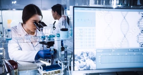 Female doctors testing samples in futuristic laboratory. Using microscopes and computer with data