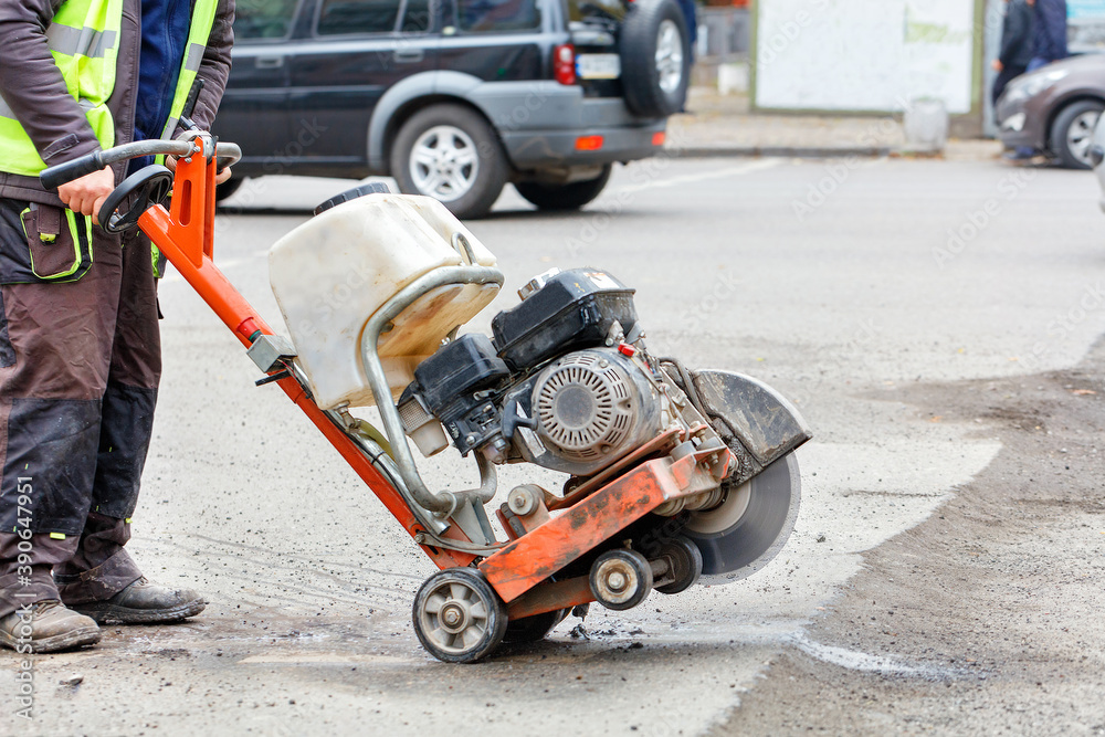 Obraz premium A worker moves a petrol cutter with a working diamond cut-off wheel to a bad section of the road that needs repair.