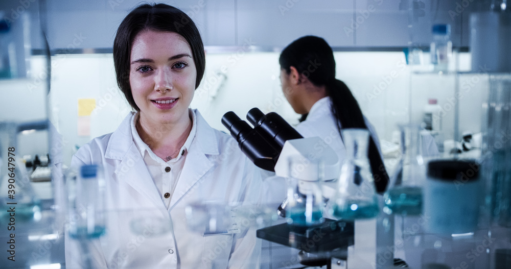 Multi ethnic science team working with microscope and computer. Female doctors in futuristic laboratory. Smiling at camera Multi ethnic science team working with microscope and computer. Female doctors in futuristic laboratory. Smiling at camera
