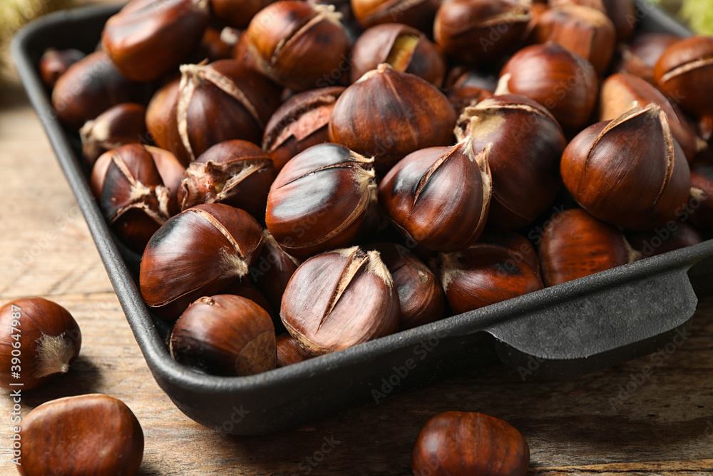 Delicious roasted edible chestnuts in baking dish on wooden table, closeup Delicious roasted edible chestnuts in baking dish on wooden table, closeup