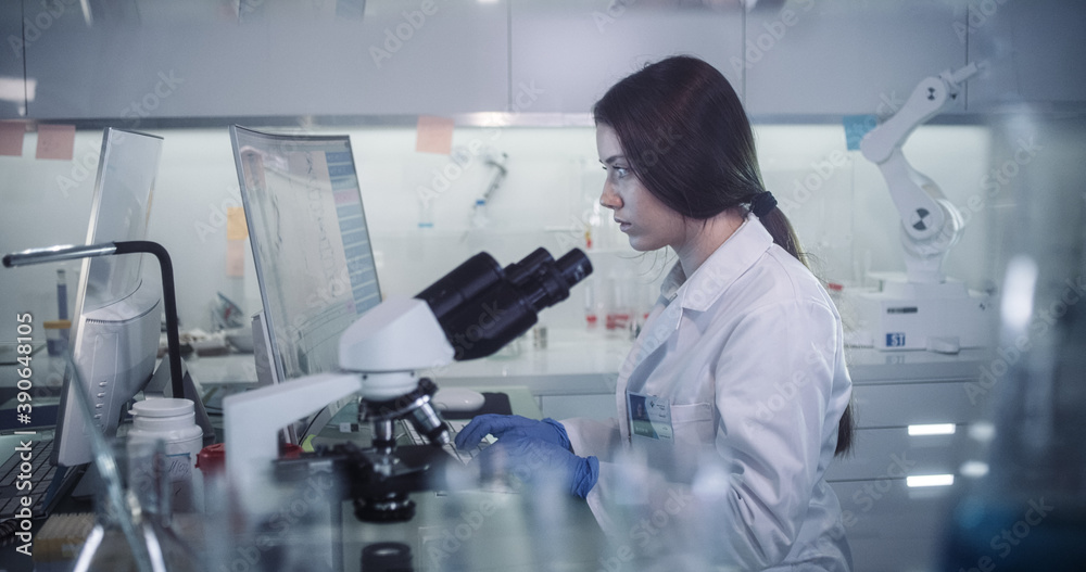 Young female doctor working with microscope. Close up on face. Futuristic laboratory interior