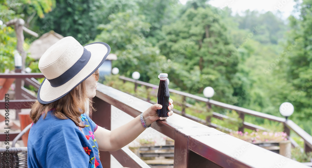 Selective focus on the bottle glass of Mulberry juice or fresh detox berry juice in a woman's hand relaxing in front of green forest nature background. Healthy drink and Refreshing beverage concept.