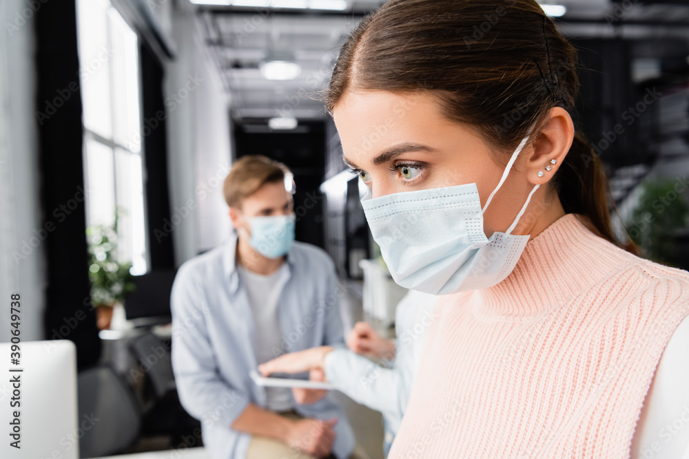 Businesswoman in medical mask standing near colleagues on blurred background in office Businesswoman in medical mask standing near colleagues on blurred background in office