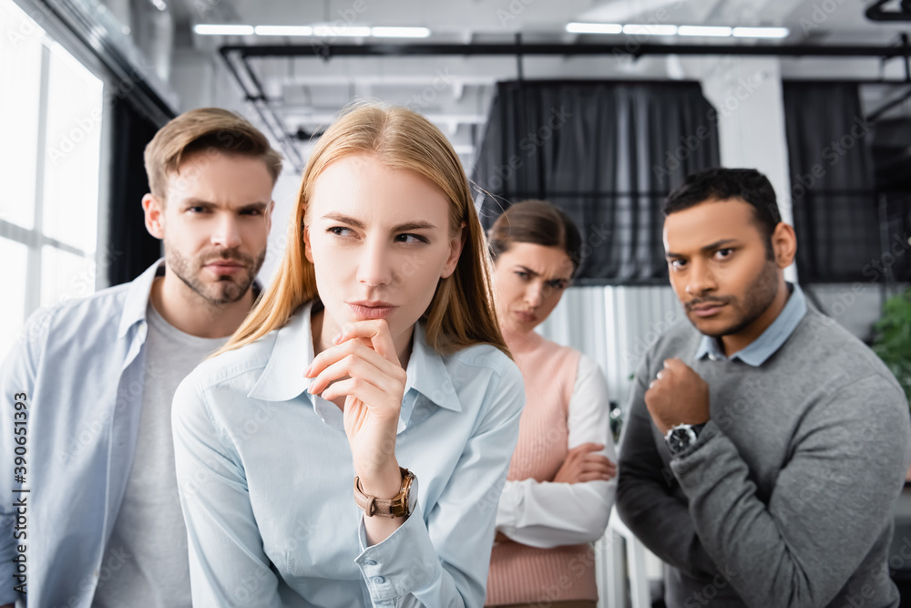 Obraz premium Pensive businesswoman standing near multiethnic colleagues on blurred background in office