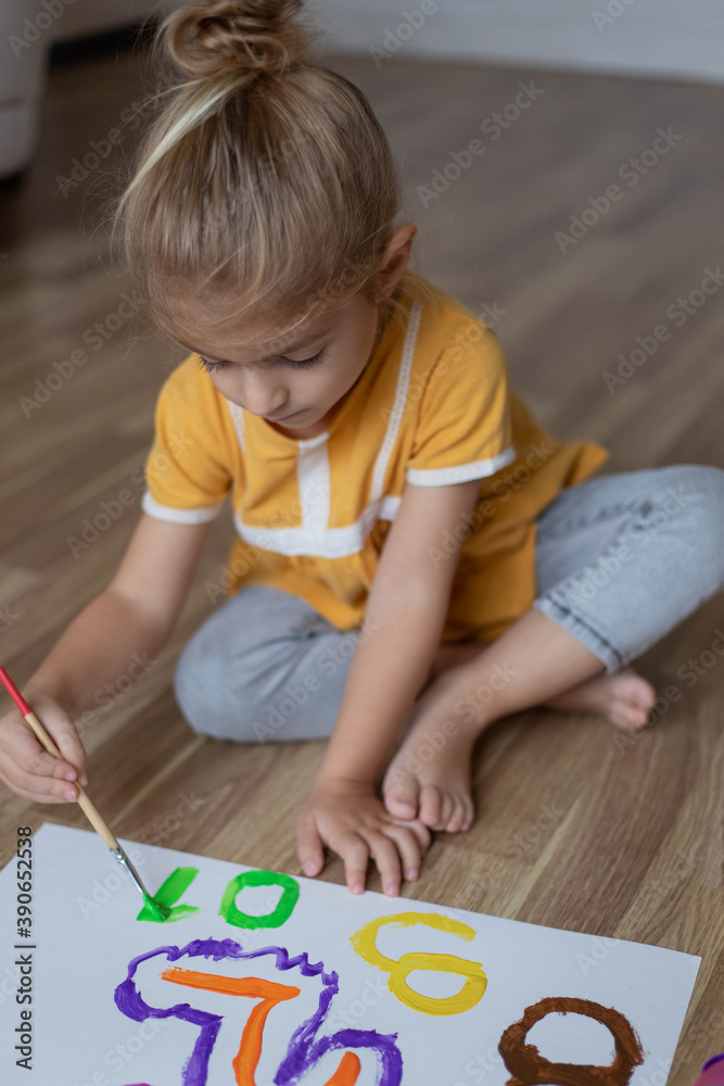Little preschool child girl sitting on warm floor and painting numbers with paints. Little preschool child girl sitting on warm floor and painting numbers with paints.
