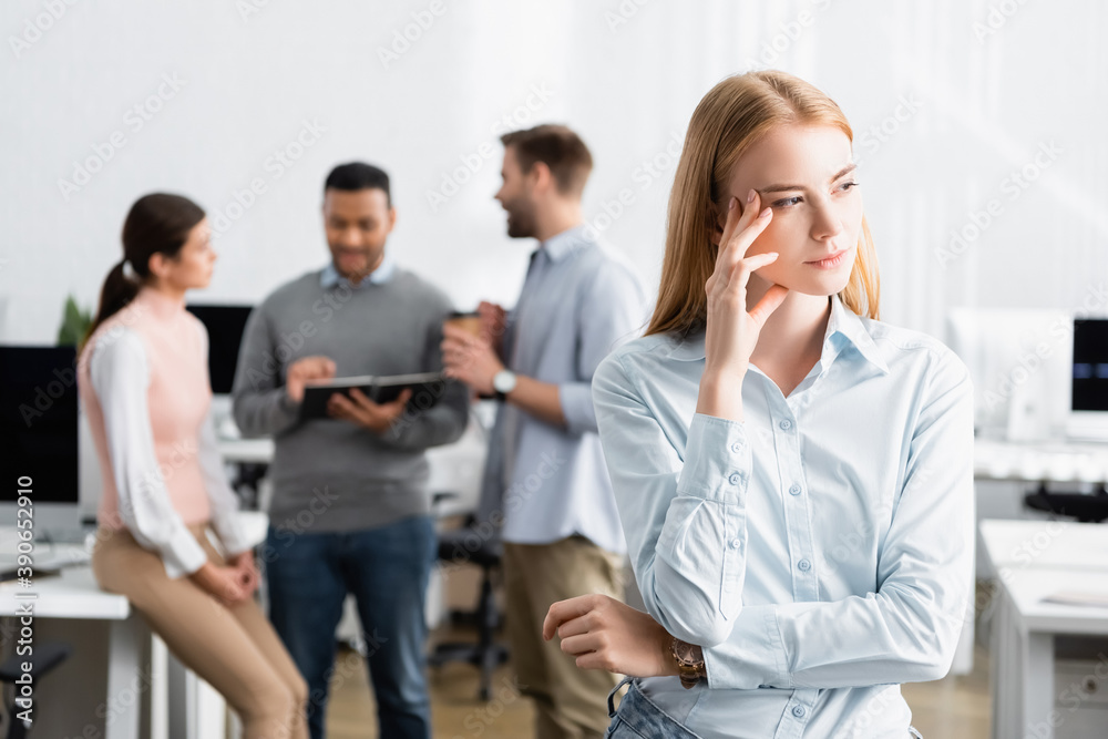 Pensive businesswoman standing near colleagues working on blurred background Pensive businesswoman standing near colleagues working on blurred background