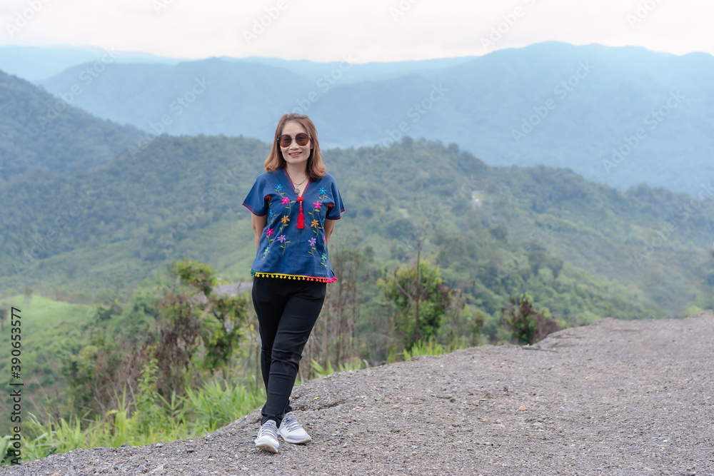 Adult traveling woman wearing sunglasses standing and smiling on the top of the mountain cliff with relaxing mood and watching beautiful view of woods and clouds foggy on vacation. Nature background Adult traveling woman wearing sunglasses standing and smiling on the top of the mountain cliff with relaxing mood and watching beautiful view of woods and clouds foggy on vacation. Nature background